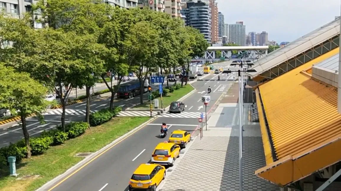 Elevated street camera view of a multi-lane road with taxis stopped at the curb